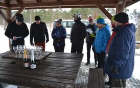Grupa dziewięciu os&oacute;b stojących pod wiatą nad stołem, na kt&oacute;rym znajdują sie kieliszki i dwa szampany