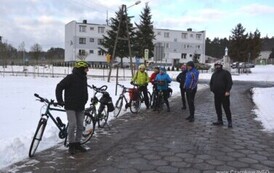 Grupa stojąca z rowerami na drodze, w tle blok mieszkalny