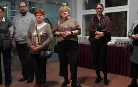 Stojących pięc os&oacute;b, w tle st&oacute;ł, na kt&oacute;rym stoją soki i kiliszki wypełnione ż&oacute;łtawym płynem