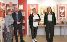 M&oacute;wiąca kobieta w asyście dw&oacute;ch innych kobiet i mężczyzny na tle ściany z grafikami białych orł&oacute;w oraz gablot z książkami
