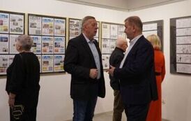 Dw&oacute;ch rozmawiających mężczyzn na tle dw&oacute;ch kobiet i mężczyzny oglądających plansze z gazetowymi stronami i grafikami