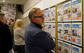 Grupa os&oacute;b w pomieszczeniu, na ścianach kt&oacute;ego zawieszono plansze z gazetowymi stronami i grafikami