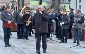 Mężczyzna stojący przed orkiestra dętą i m&oacute;wiący do mikorofonu