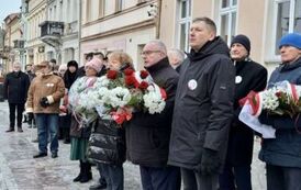 Grupa os&oacute;b stojąca z wiązankami kwiat&oacute;w
