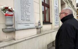 Mężczyzna stojący przed tablicą pamiątkową wmurowaną w fasadę budynku