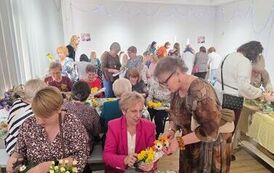 Grupa kobiet siedząca przy stole i układająca kwiaty
