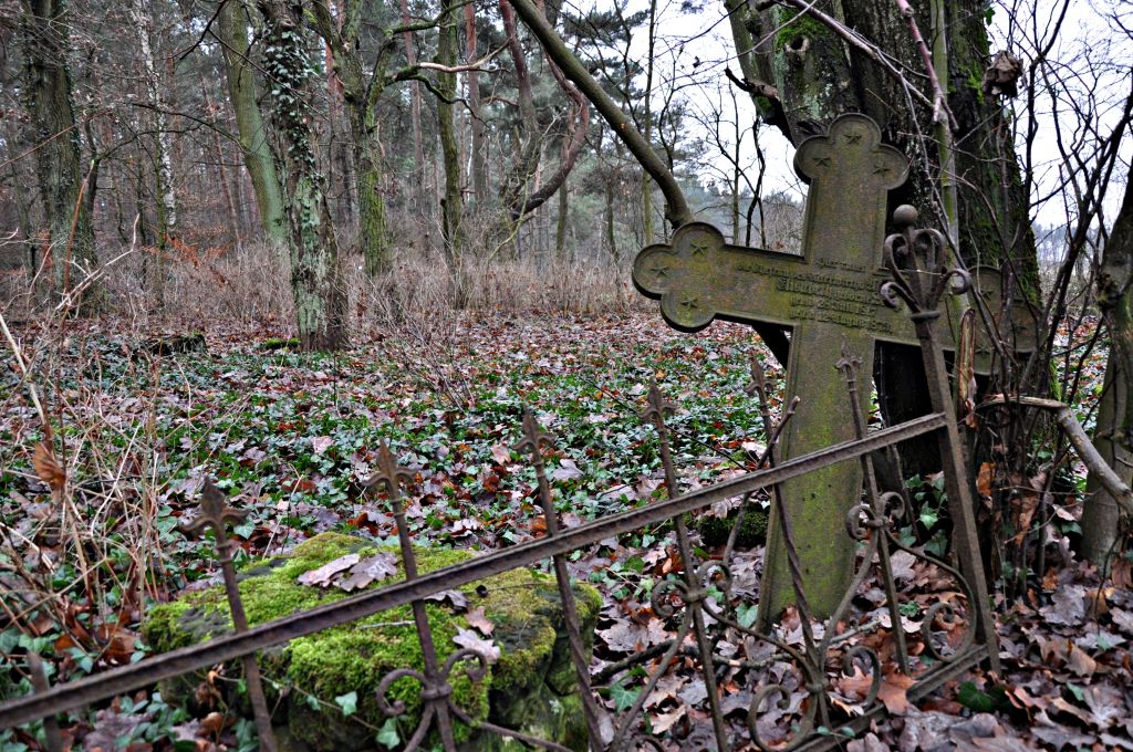 Przechylony krzyż obok nagrobka za metalowym płotem