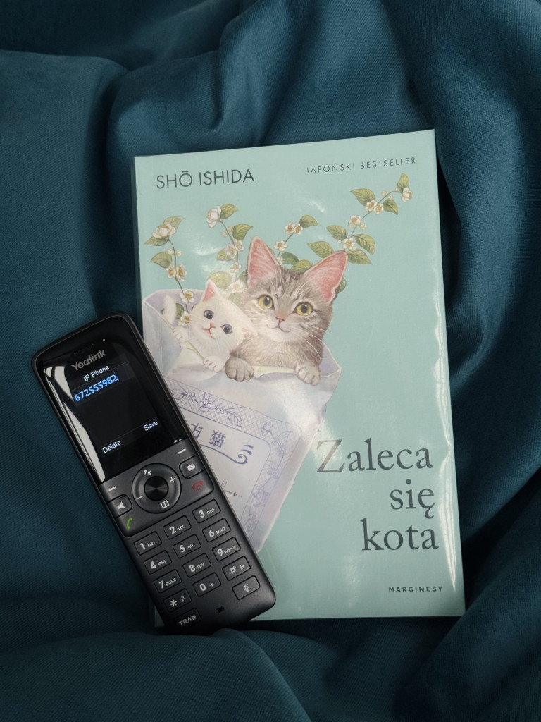 Telefon umieszczony przy książce pod tytułem "Zaleca się kota" z&nbsp;kotem na&nbsp;okładce autorstwa Sho Ishida