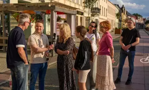 Wsród grupy siedmiu osób mężczyzna trzymający mikrofon
