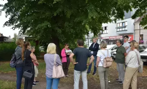 Grupa jedenastu osób zebranych wokół przewodniczki trzymającej fotografię