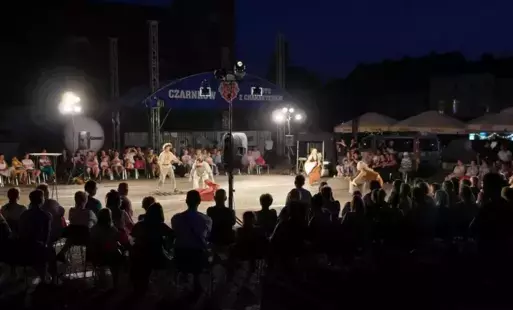 Widzowie zebrani dookoła fragmentu placu oglądający przedstawienie teatralne