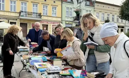 Gupa osób pochylona nad stołem wyłożonym książkami