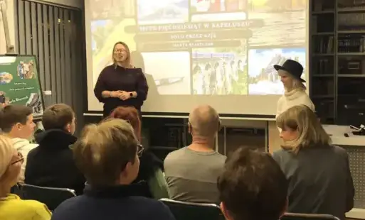 Dwie kobiety stojące na tle obrazu rzutnika przed siedzącymi ludźmi
