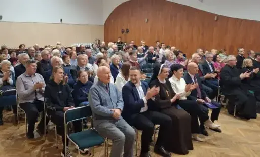 Osoby siedzące na krzsełkach ustawionych rzedami w dużej sali