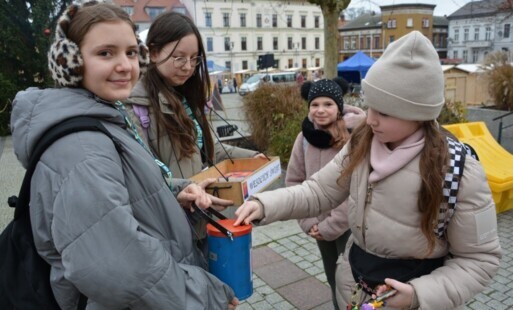 Cztery dziewczynki, z których jedna wrzuca pieniądze do puszki trzymanej przez drugą