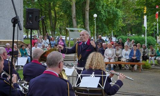 Muzycy orkiestry dętej z kapelmistrzem na tle słuchaczy
