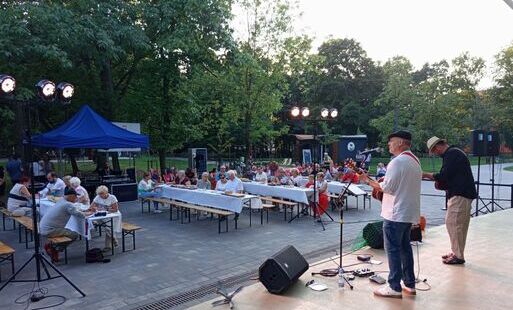 Dwóch mężczyzn z gitarami na scenie przed widownią siedzącą na plażowych leżakach