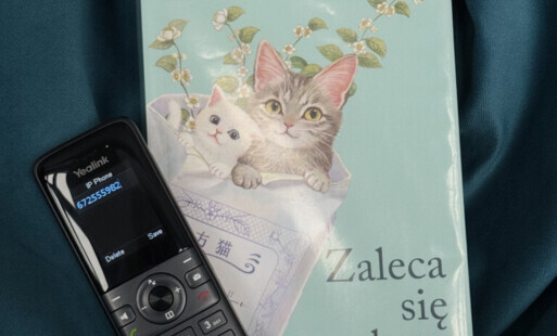Telefon umieszczony przy książce pod tytułem "Zaleca się kota" z kotem na okładce autorstwa Sho Ishida